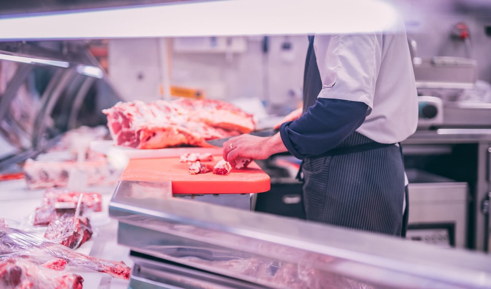 A butcher slicing meat carefully on a clean preparation bench